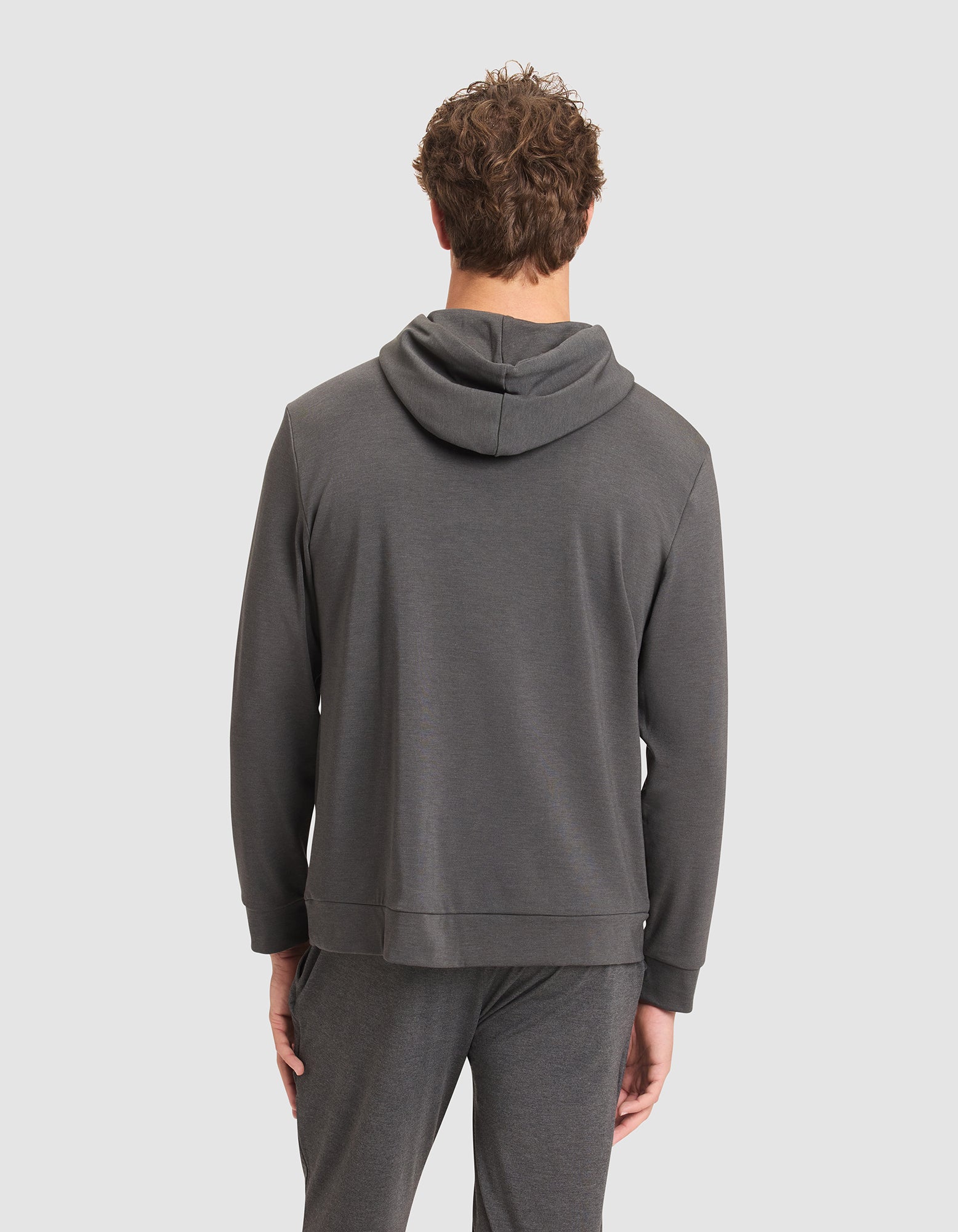 A person with short, curly hair is seen from behind wearing the Cozy Earth Men's Brushed Bamboo Hoodie in dark gray against a plain light background. 