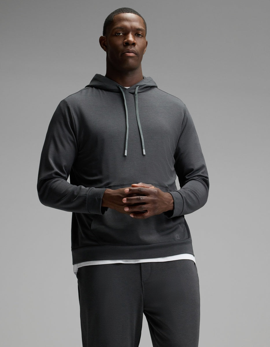 A man stands against a plain gray background wearing the Cozy Earth Men’s Brushed Bamboo Hoodie & Jogger Set, with his hands clasped together in front of him.