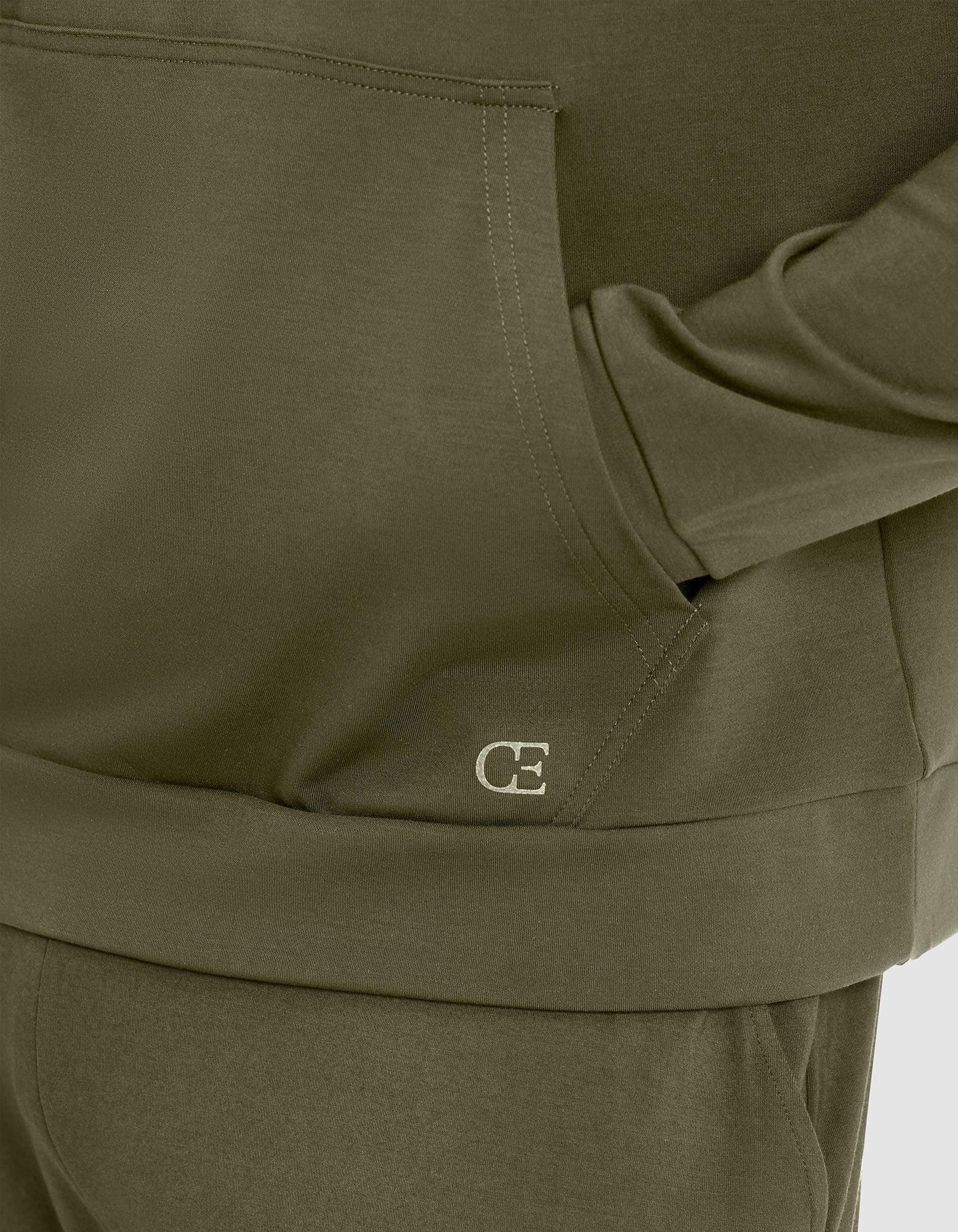 Close-up of a person wearing Cozy Earth's Men's Brushed Bamboo Hoodie in olive green, featuring matching pants and "CE" initials stitched in white near the front pocket. 
