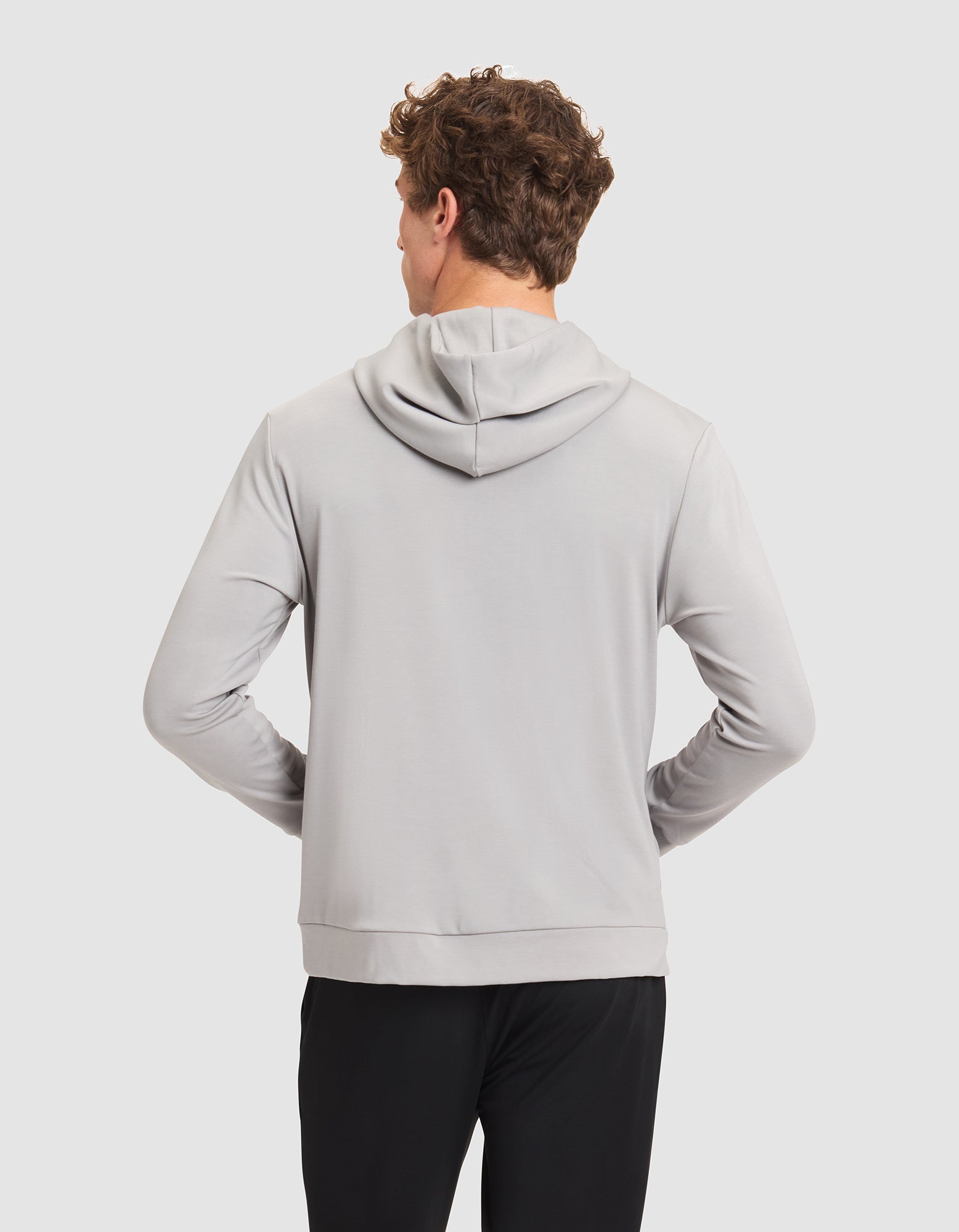 A man with short curly hair is seen from behind in a Cozy Earth Men's Brushed Bamboo Hoodie, light gray, paired with black pants against a plain light background. 