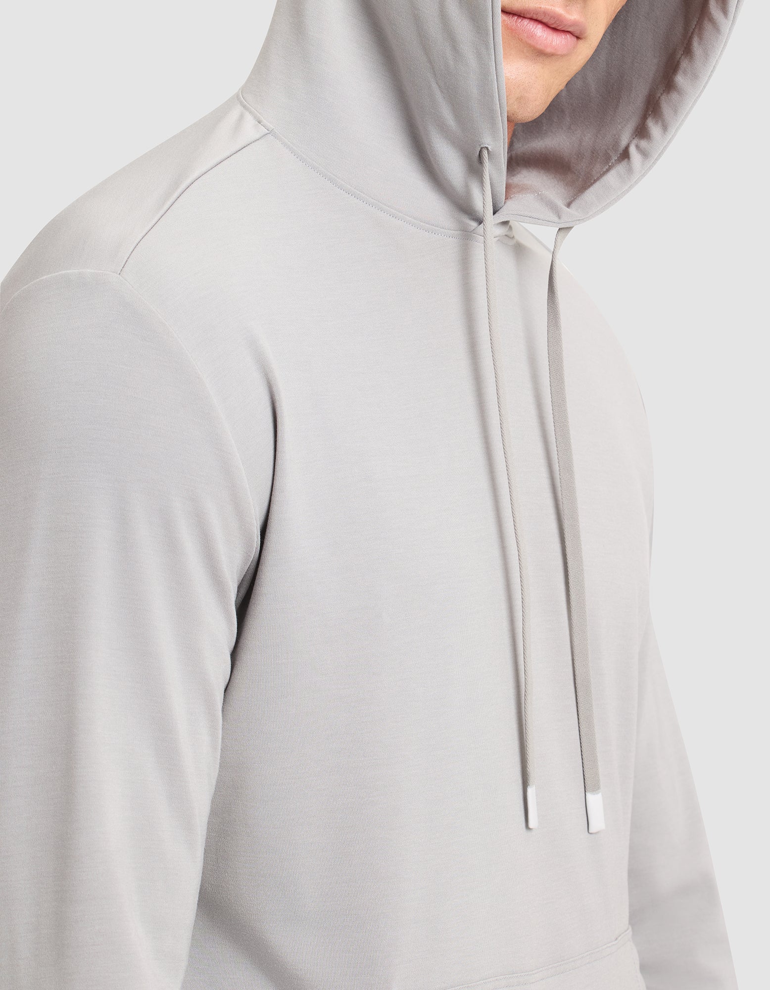 A man wears the Cozy Earth Men's Brushed Bamboo Hoodie in light gray, hood up with drawstrings down, shown from the chest up with his face partially visible. 