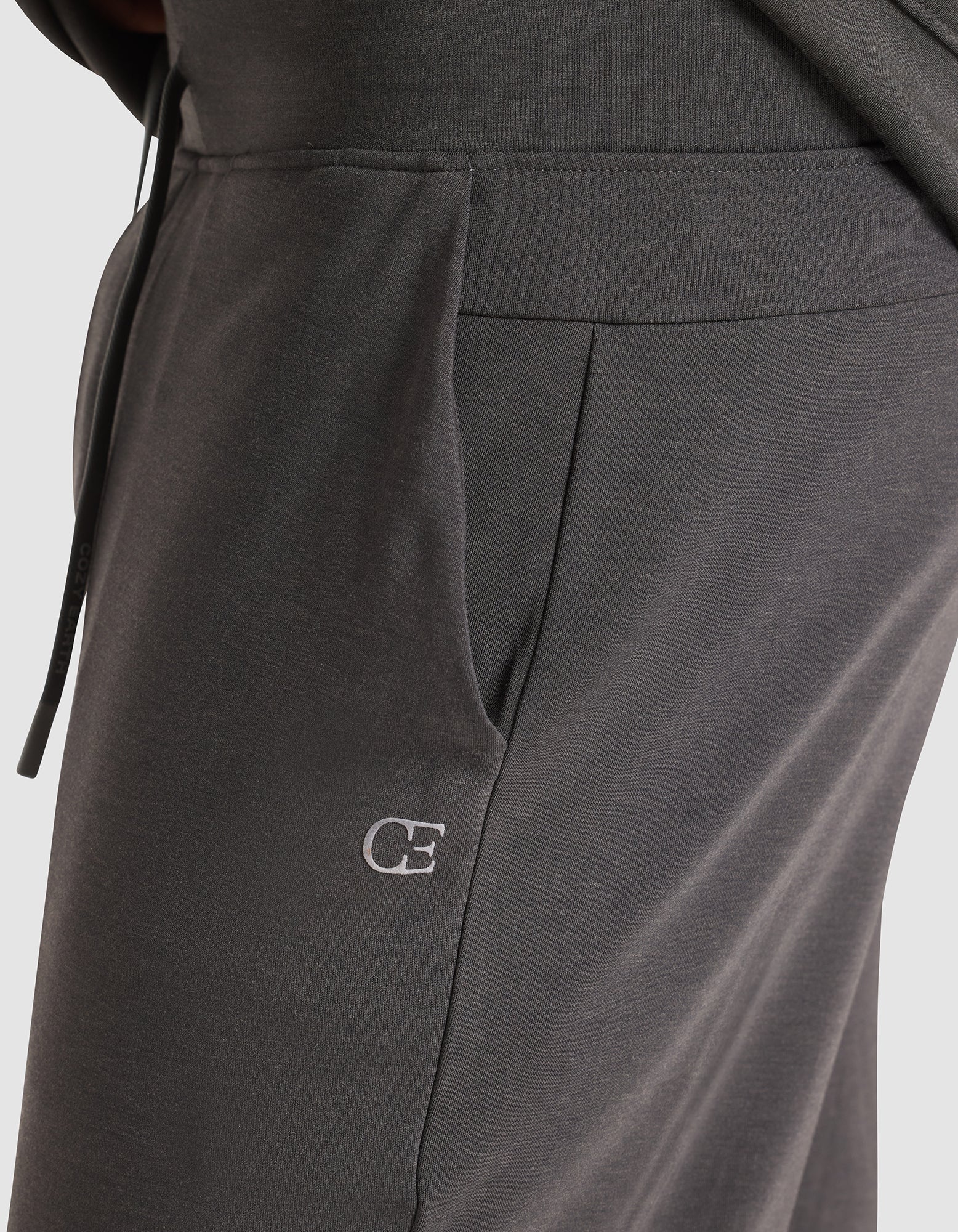 Close-up of a person wearing Cozy Earth's Men's Brushed Bamboo Jogger Pant in dark gray, featuring a visible side pocket and an embroidered white "CE" logo near the pocket. 