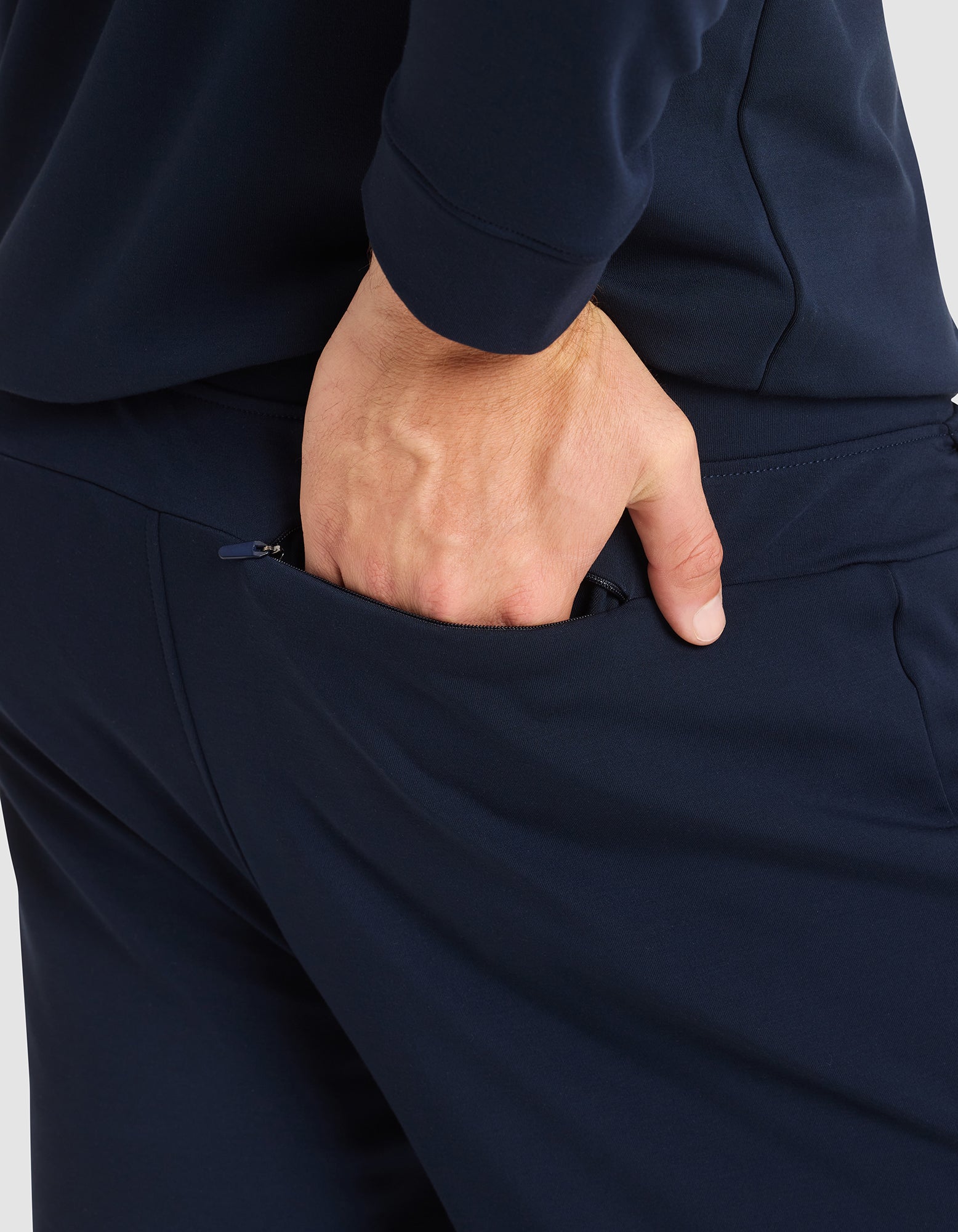A close-up shows a person wearing Cozy Earth's Men's Brushed Bamboo Jogger Pant in navy blue, placing their right hand in the back pocket, highlighting the hand and pocket area. 