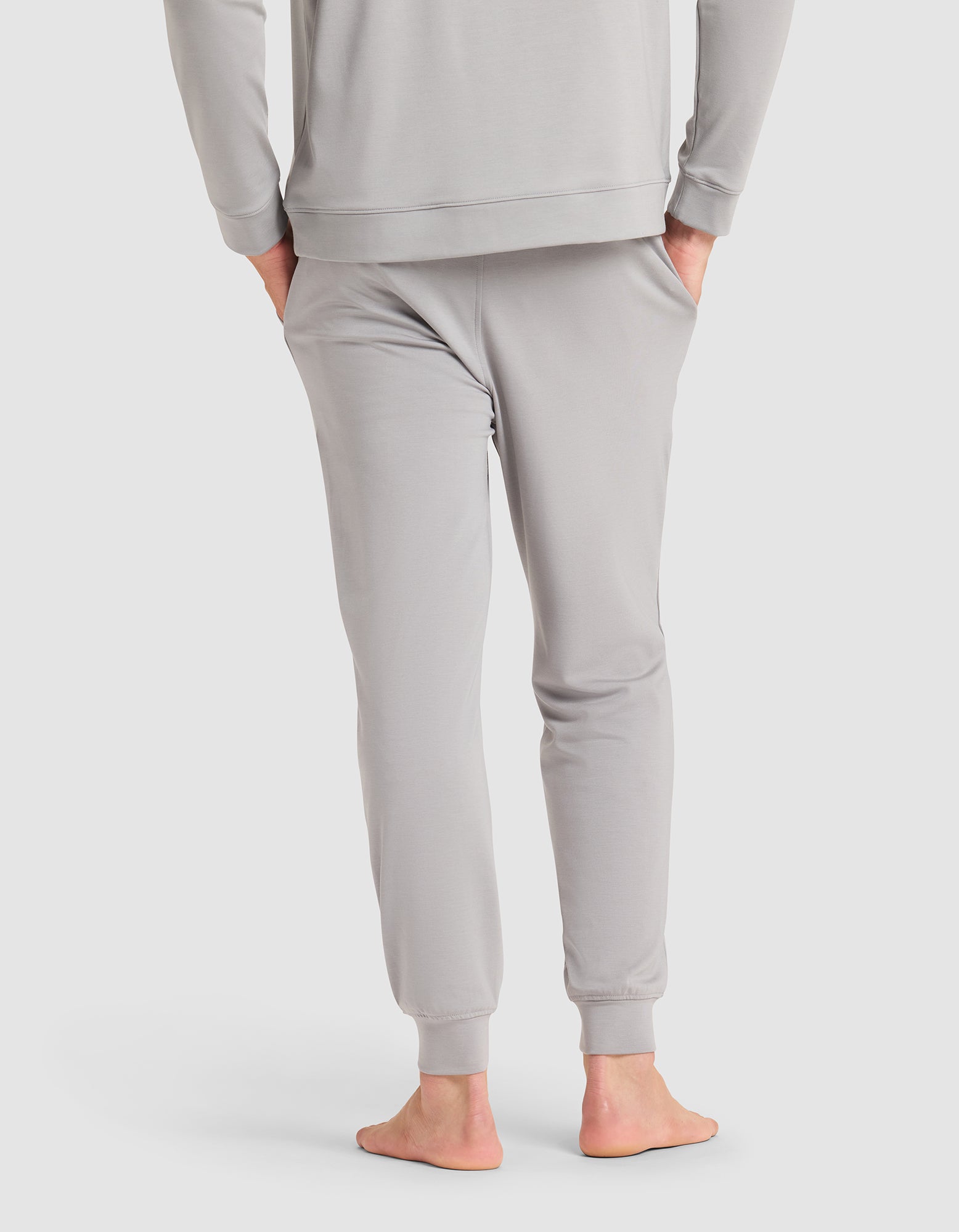 A barefoot man, seen from behind, wears Cozy Earth's Men's Brushed Bamboo Jogger in light gray with a matching long-sleeve top. 