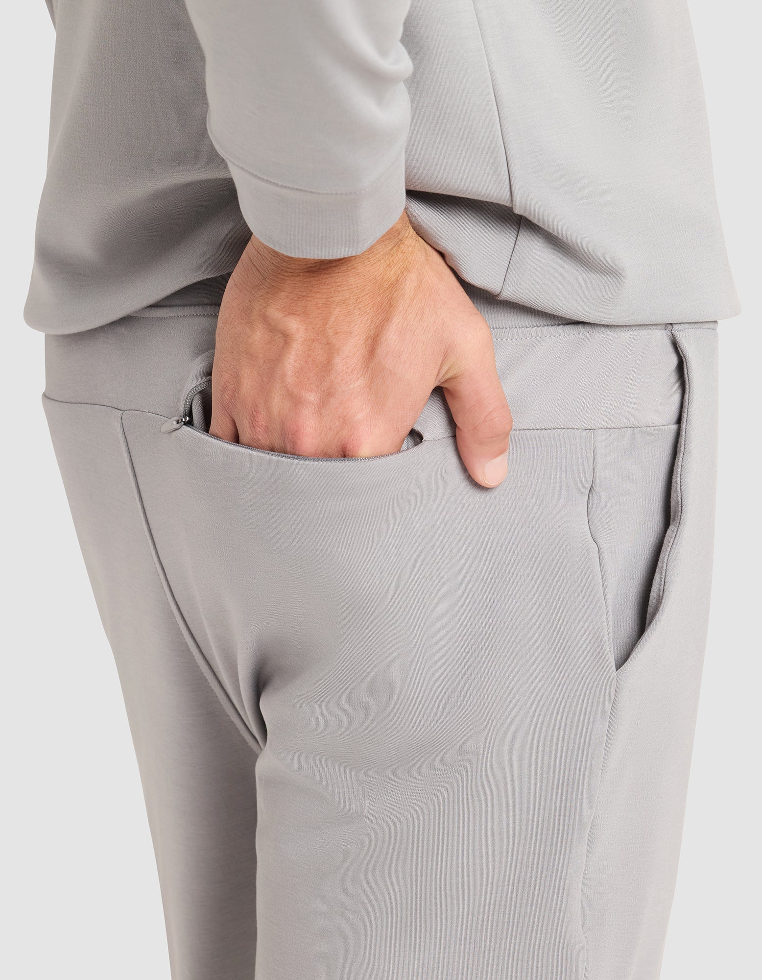 A person is shown from the waist down wearing Cozy Earth Men's Brushed Bamboo Jogger Pant in light gray, with a matching long-sleeve shirt and their right hand tucked into their pants pocket. 