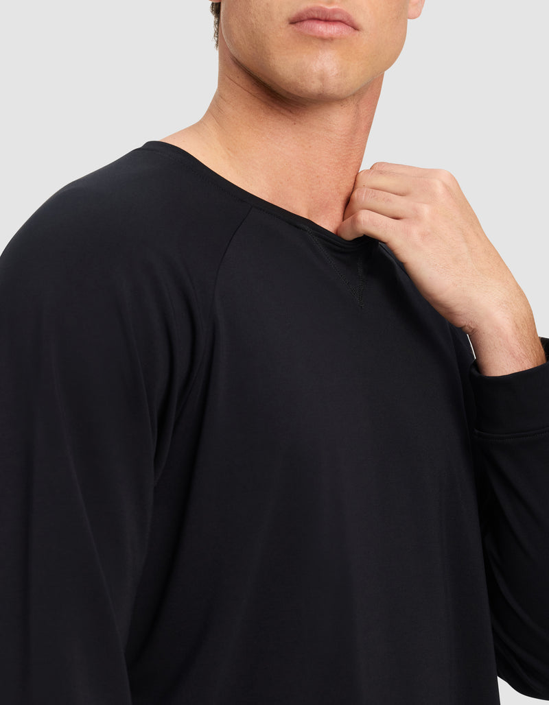 A man, his face partially visible, stands against a plain light background wearing the Cozy Earth Men's Brushed Bamboo Pullover Crew in black, with one hand touching the shirt's collar.