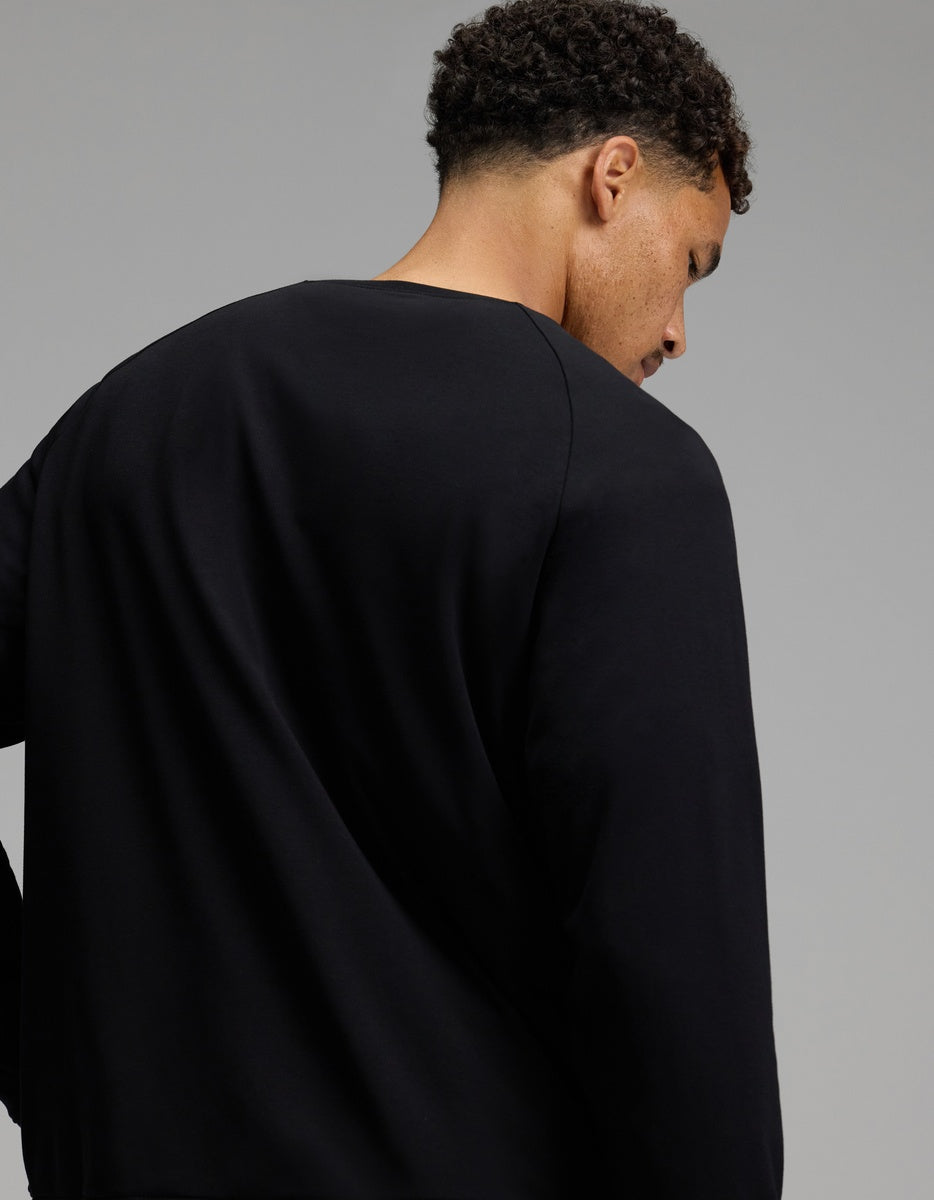 A person with short curly hair is shown from behind, wearing the Cozy Earth Men’s Brushed Bamboo Pullover Crew in plain black, standing against a neutral gray background.