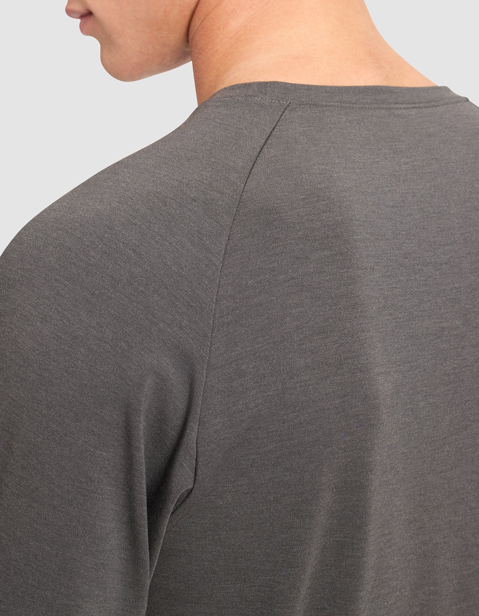 Close-up of a person wearing the Cozy Earth Men's Brushed Bamboo Pullover Crew in dark gray, showing the upper back, shoulder, and part of the neck and jawline against a plain light background.  