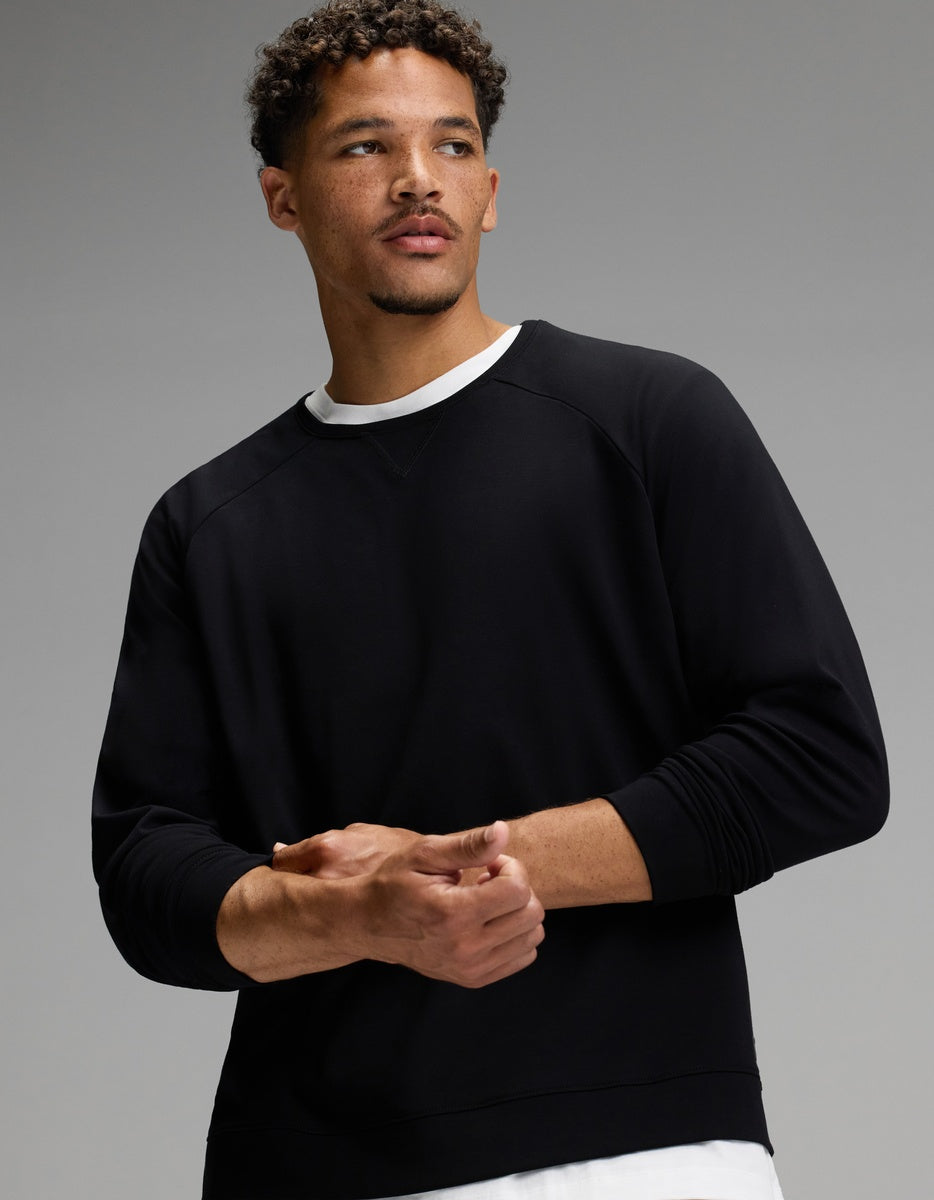 A man with short curly hair and a trimmed beard models the Cozy Earth Men’s Brushed Bamboo Jogger Set in black, layered over a white undershirt, as he stands against a gray background and looks to the side.