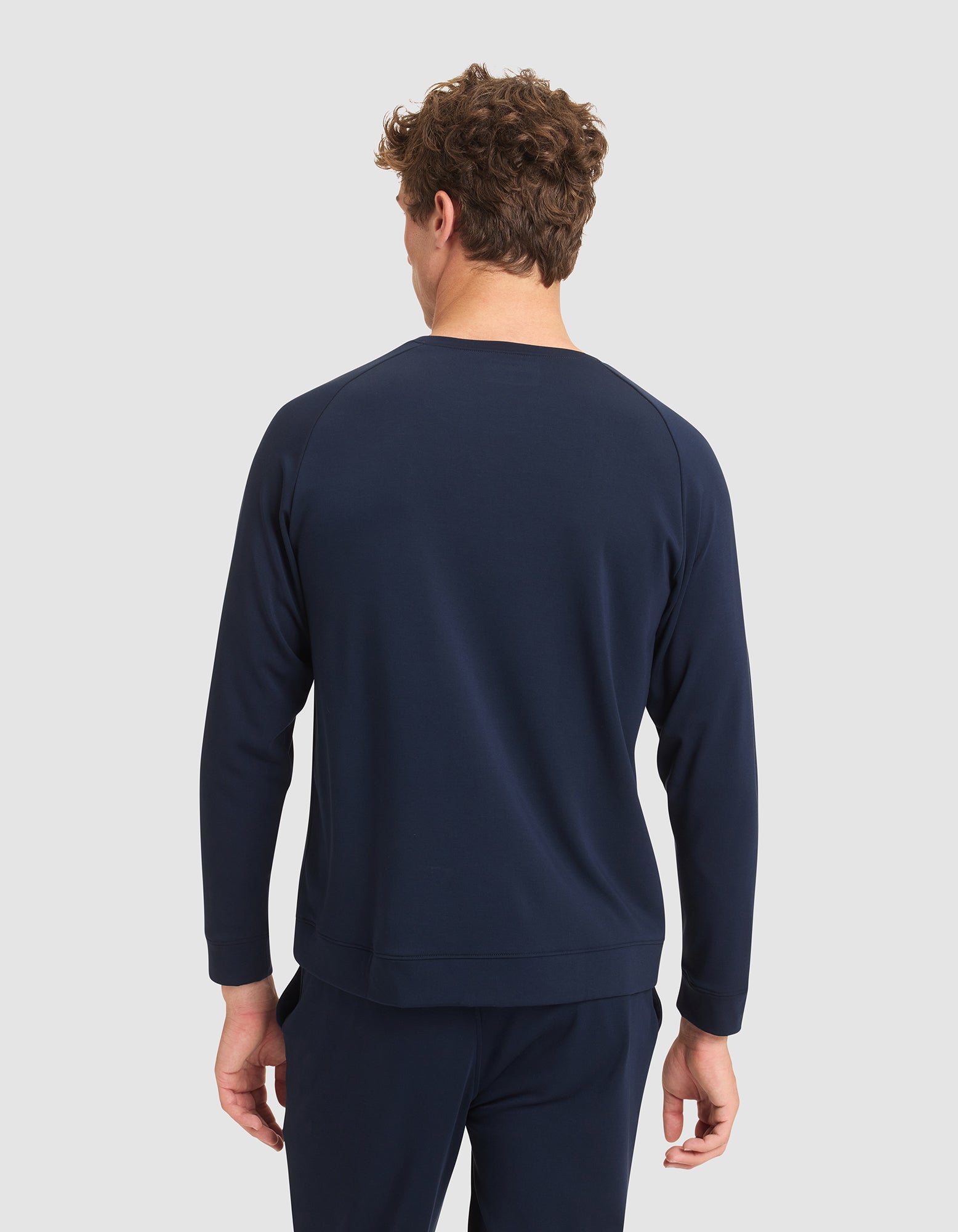 A man with curly hair is seen from behind, wearing the Cozy Earth Men's Brushed Bamboo Pullover Crew in navy blue against a plain light gray background. 