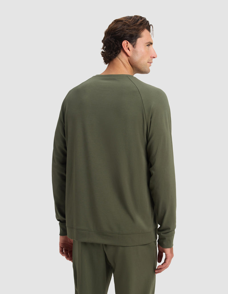 A man stands facing away, wearing the Cozy Earth Men's Brushed Bamboo Pullover Crew in olive green, paired with matching pants, set against a plain light gray background.