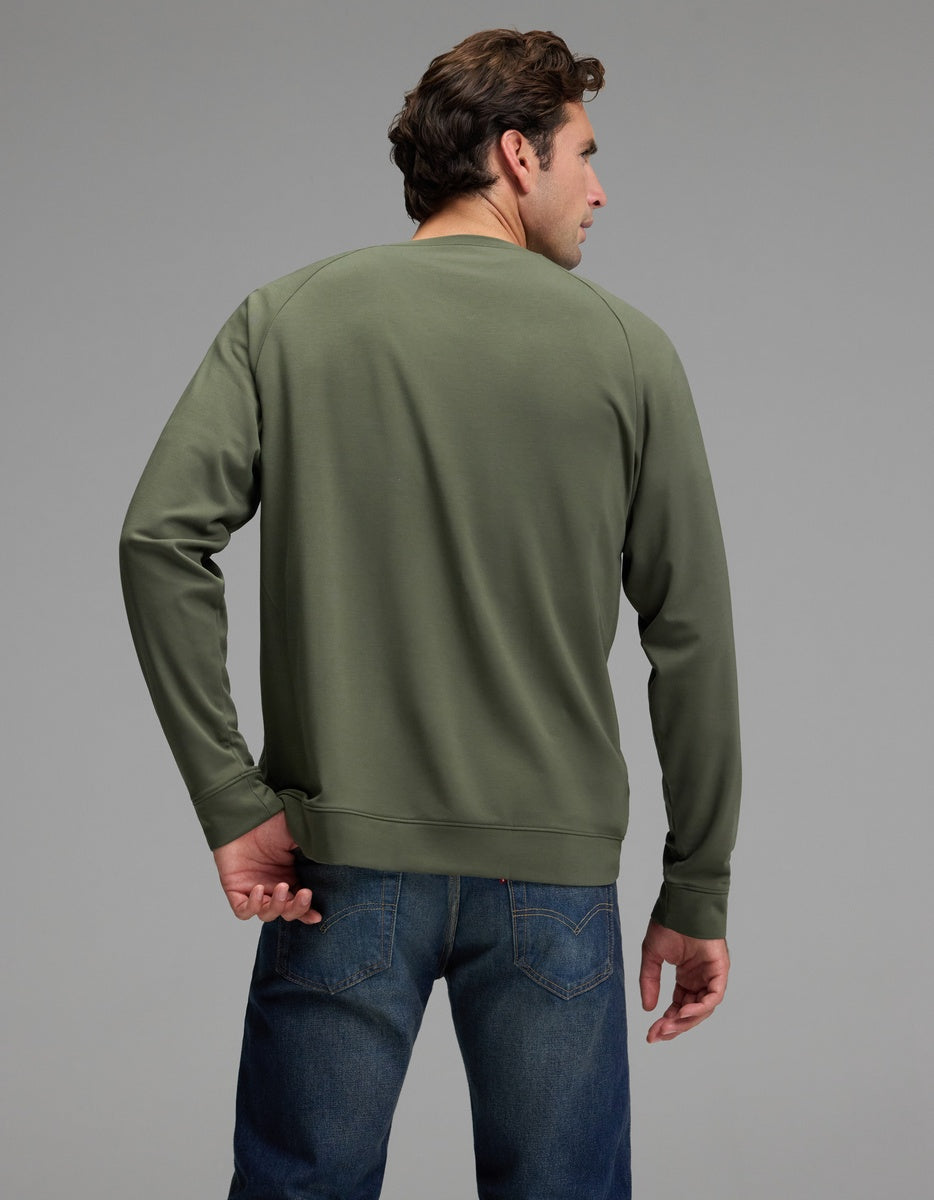 A man is seen from behind, his head turned slightly to the left, wearing the Cozy Earth Men’s Brushed Bamboo Pullover Crew in olive green and blue jeans, set against a plain gray background.
