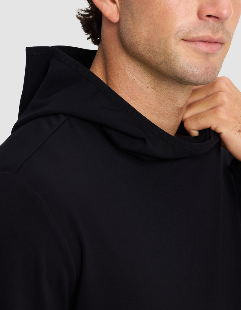 A close-up shows a person wearing the Cozy Earth Men's Brushed Bamboo Recovery Hoodie in black, gently holding the hood's edge near their neck, with their face partially visible and a slight smile.