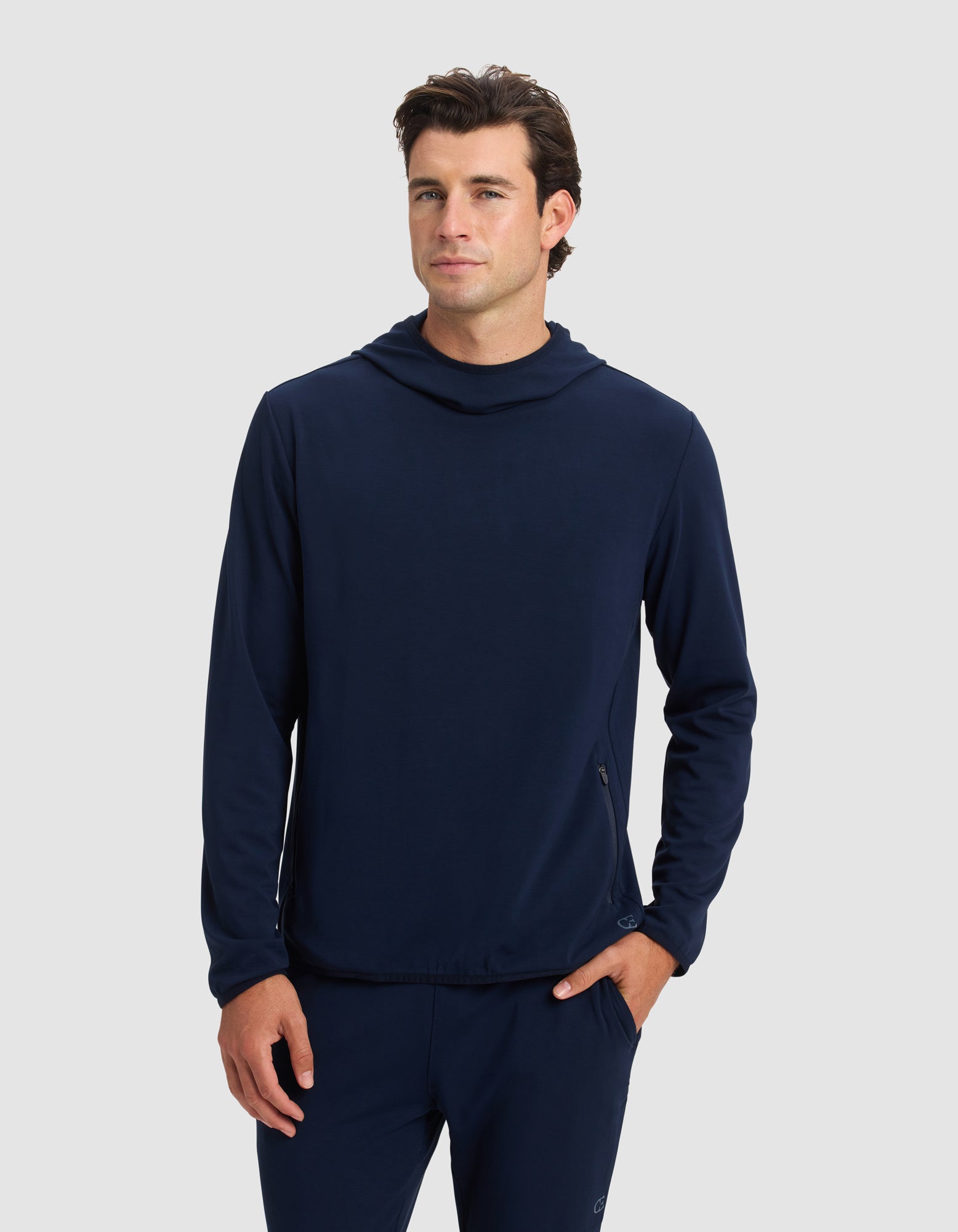 A man stands facing forward with one hand in his pocket, wearing the Cozy Earth Men's Brushed Bamboo Recovery Hoodie and matching pants against a plain light gray background. 