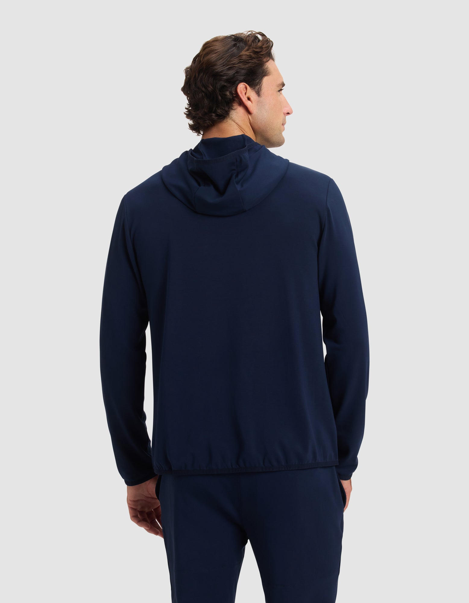 A man with short brown hair stands with his back to the camera against a light gray background, wearing the Cozy Earth Men's Brushed Bamboo Recovery Hoodie in navy blue. 