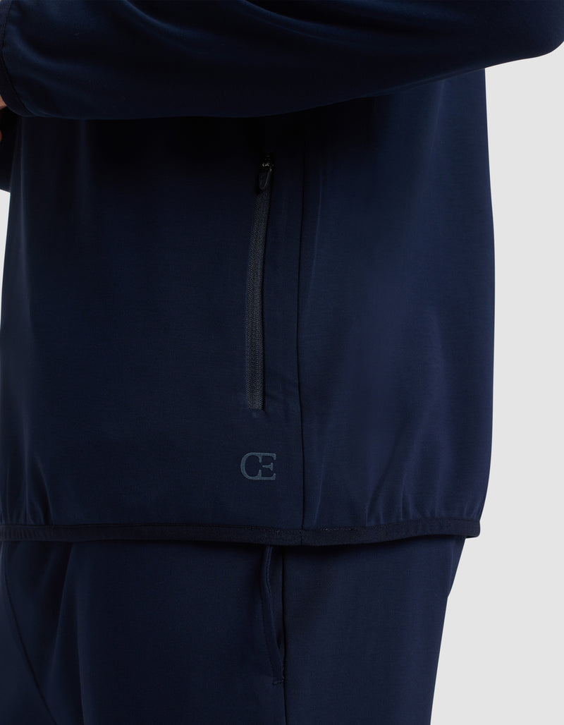 A close-up of a person wearing the Cozy Earth Men's Brushed Bamboo Recovery Hoodie in dark blue. The hoodie features a vertical zippered pocket and a small "CE" logo near the hem. Only the torso and upper legs are visible.