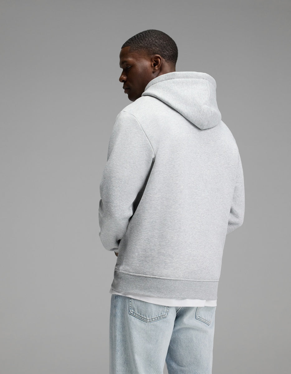 A person wearing the Cozy Earth Men’s Cityscape 2.0 Hoodie in light gray and light blue jeans stands facing away from the camera against a plain gray background.