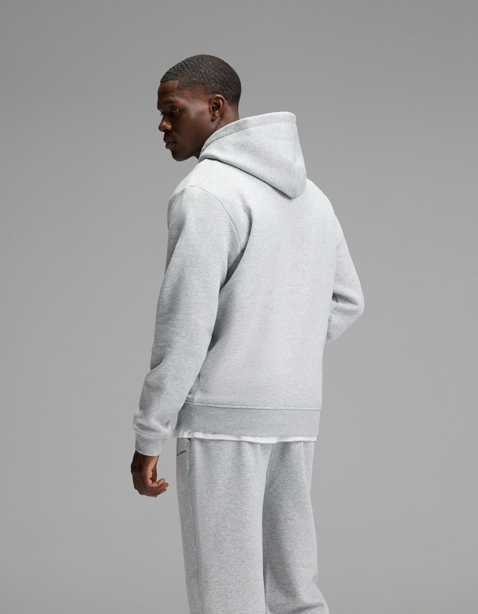 A man models the Cozy Earth Men’s Cityscape 2.0 Hoodie & Sweatpant Set in light gray, standing against a plain gray background and glancing over his left shoulder.