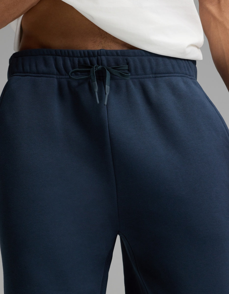 A person wearing a white shirt and Cozy Earth’s Men’s Cityscape 2.0 Sweatpant in navy blue; the image is cropped to show only the lower torso and upper legs.