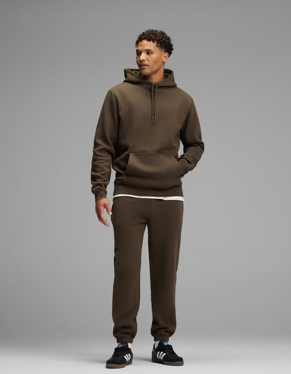 A person wearing a dark brown Men’s Cityscape Hoodie & Sweatpant Set over a white undershirt.