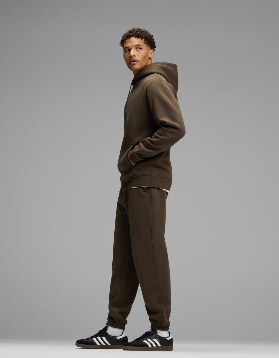 A man wearing a dark olive Men’s Cityscape Hoodie & Sweatpant Set consisting of a matching hoodie and sweatpants.