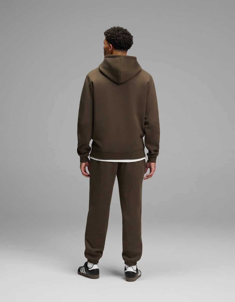 A person seen from behind wears a brown Men’s Cityscape Hoodie & Sweatpant Set over a white shirt, paired with black sneakers.