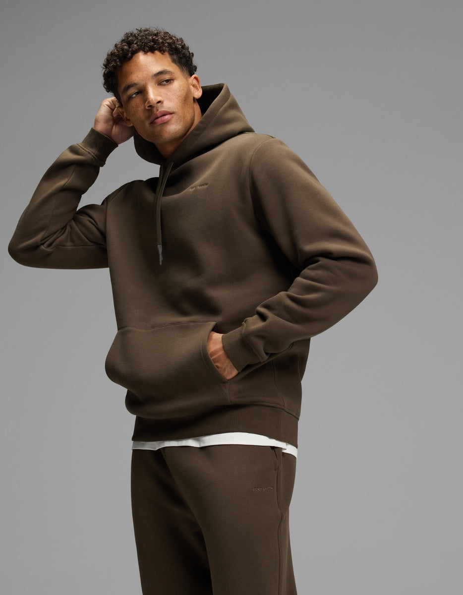A man wearing a dark olive green Men’s Cityscape Hoodie and matching sweatpants.