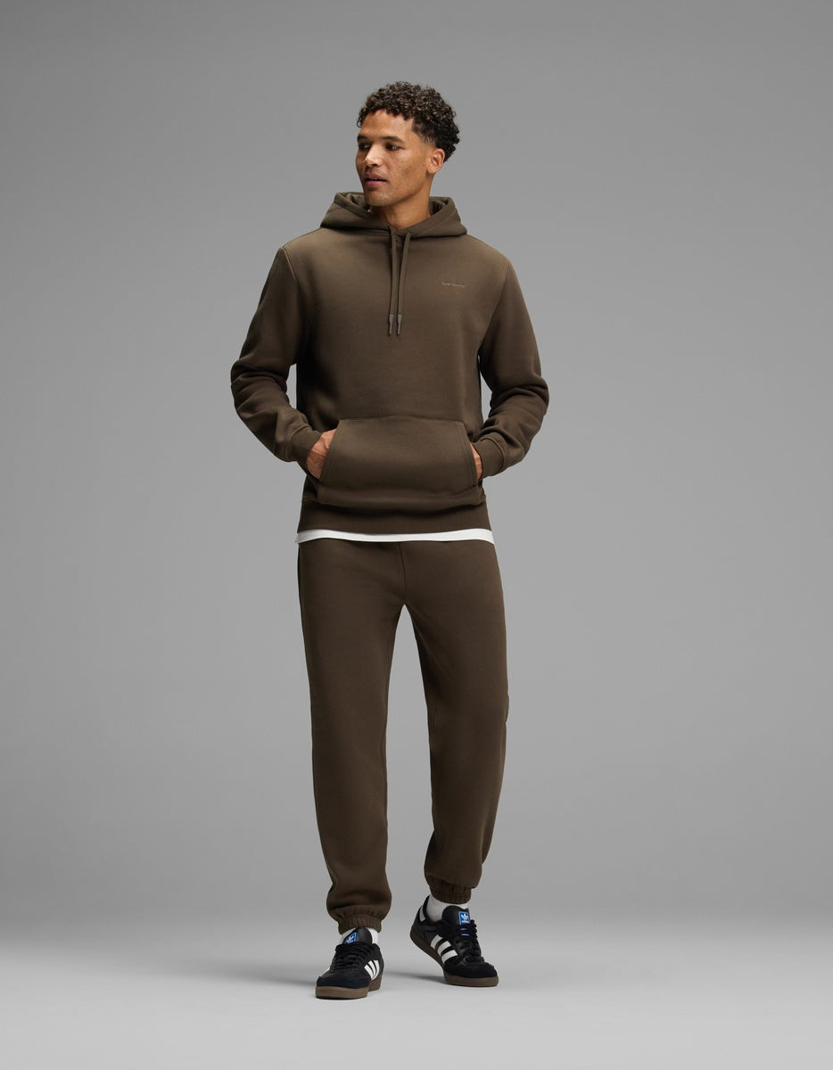 A man wearing a brown Men’s Cityscape Hoodie and matching sweatpants over a white undershirt, with dark sneakers.