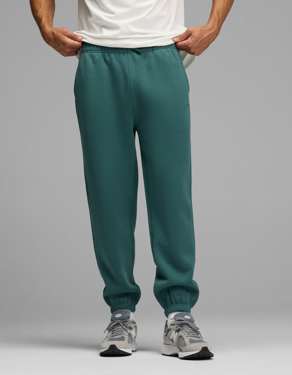 A person wearing dark green Men’s Cityscape Sweatpant joggers with elastic cuffs and grey sneakers.