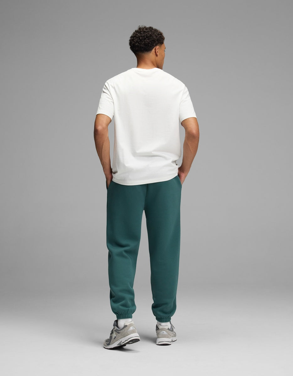 A man seen from behind wearing a white t-shirt, dark green Men’s Cityscape Sweatpant, and gray sneakers.