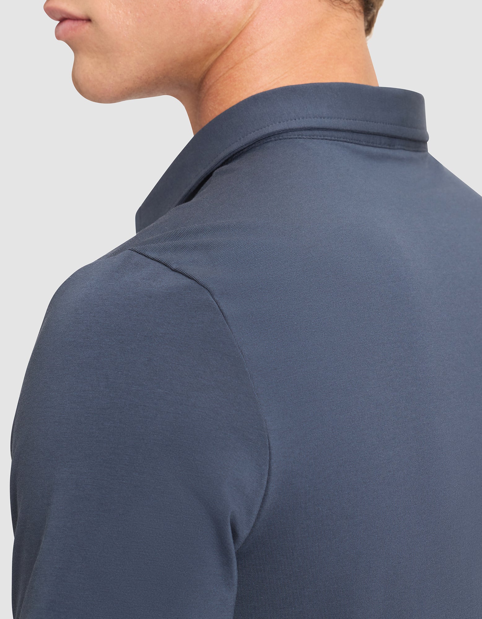 A close-up of a person wearing the Cozy Earth Men's Everyday Polo in dark blue, shown from the side and back. The image highlights the fabric, collar, and shoulder details with part of the head visible. |Color:Eclipse