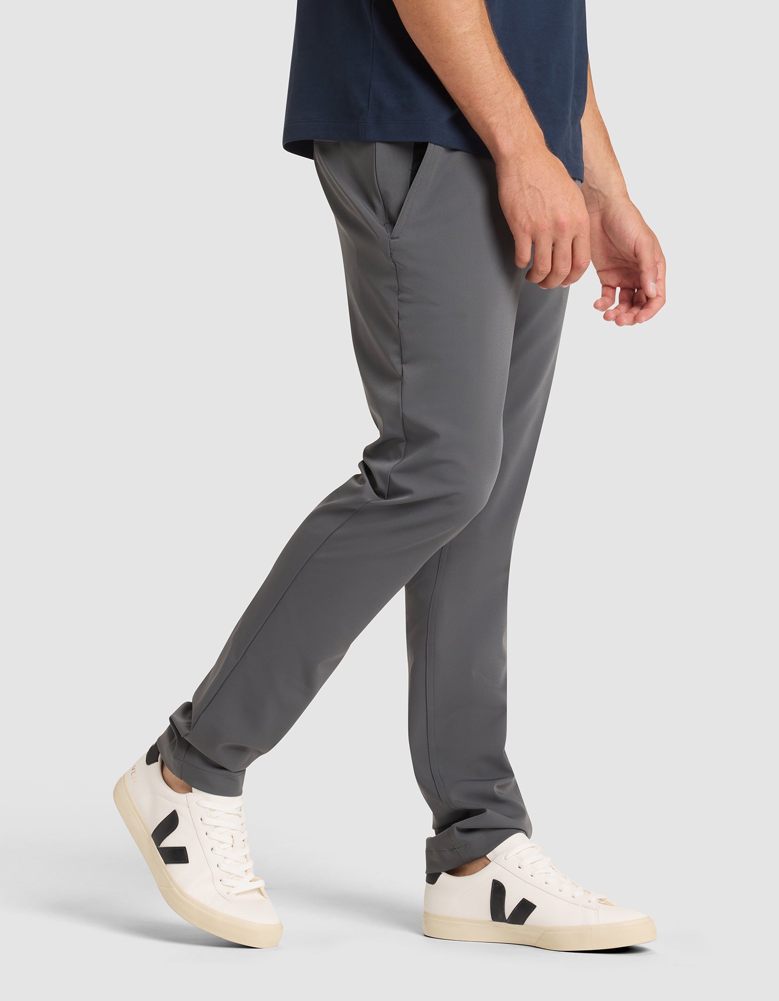 A man models the Cozy Earth Men's Everywhere Pant in gray with a navy shirt and white sneakers featuring black "V" logos, standing against a plain gray background, shown from shoulder to feet.  