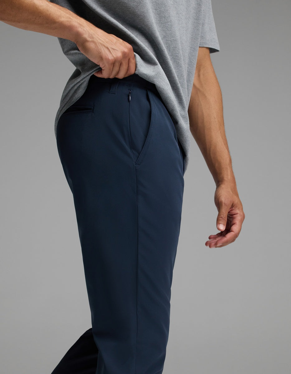 A person wearing a grey shirt and navy blue Cozy Earth Men’s Everywhere Pant stands with one hand lifting the shirt slightly, revealing the waistband and top of the pants.