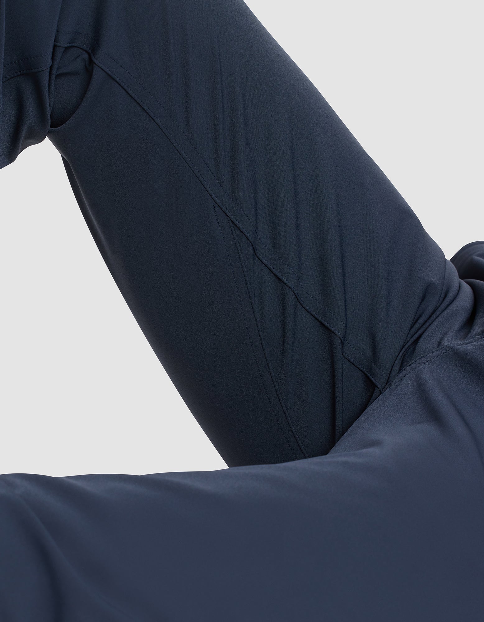 Close-up of a person wearing Cozy Earth Men's Everywhere Pant in dark navy blue, with a bent knee and leg partially visible against a light gray background. 