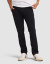 A person wearing Cozy Earth's Men's Everywhere Pant in black, a white t-shirt, and cream-colored sneakers with black detailing stands with hands in pockets against a plain light background. |Color:Jet Black