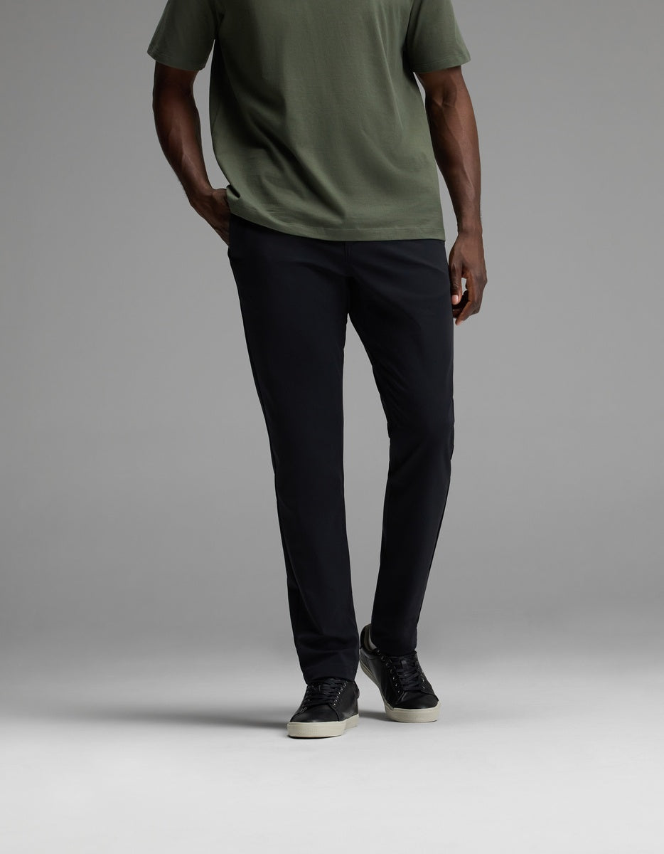 A person wearing Cozy Earth’s Men’s Everywhere Pant in black, paired with a short-sleeve olive green shirt and black sneakers with white soles, stands against a plain gray background. Their face is not visible.|Color:Jet Black