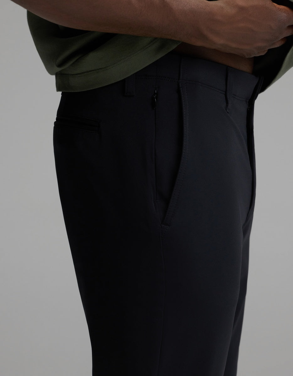 A person wearing Cozy Earth’s Men’s Everywhere Pant in black and a green shirt stands with one hand near the waistband, highlighting a close-up side view of the pant’s pocket and tailored fit.