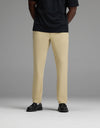 A person wearing the Cozy Earth Men’s Everywhere Pant in beige, paired with a black short-sleeve shirt and black shoes, stands against a plain gray background. Their head is not visible in the image.|Color:Khaki
