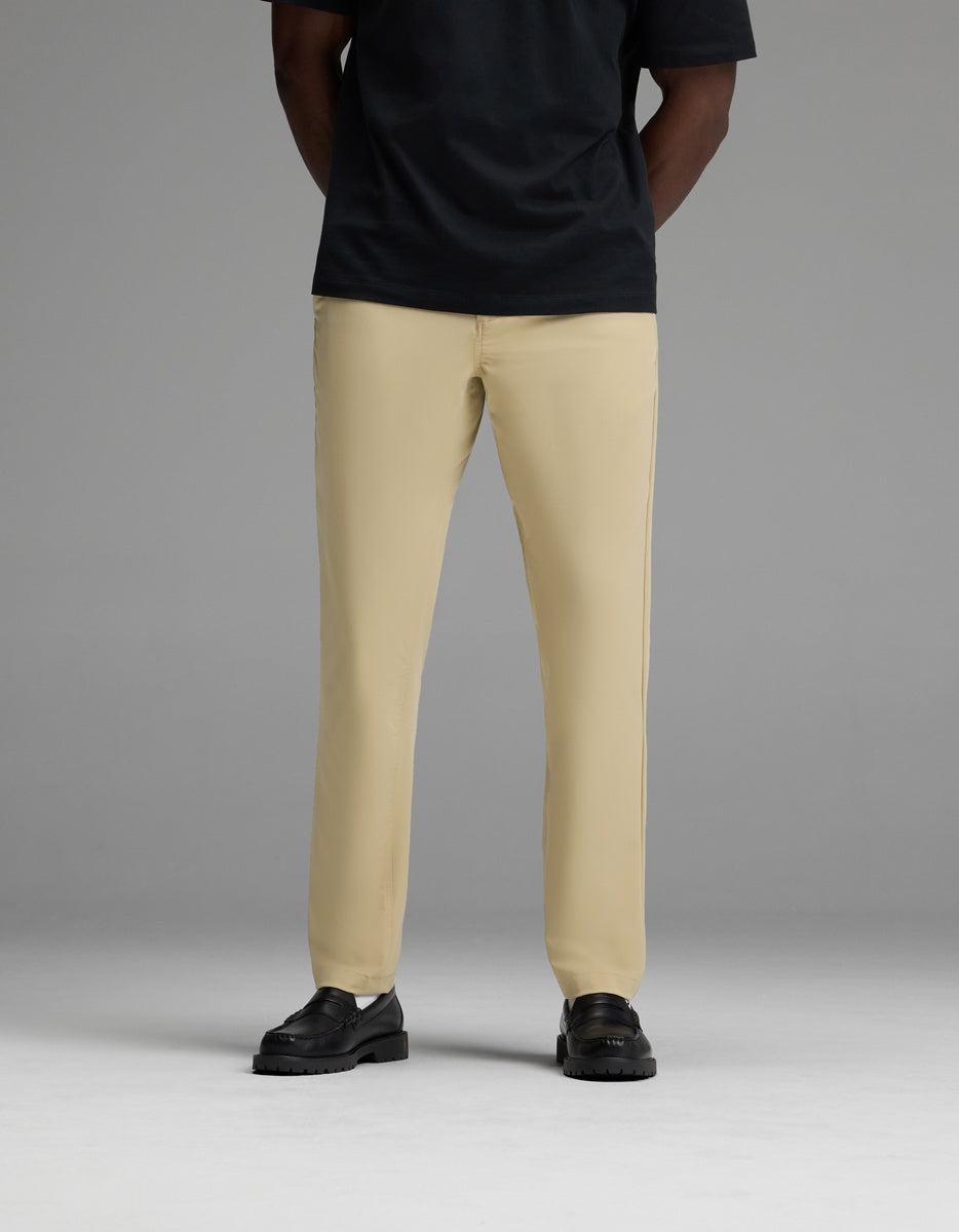 A person wearing the Cozy Earth Men’s Everywhere Pant in beige, paired with a black short-sleeve shirt and black shoes, stands against a plain gray background. Their head is not visible in the image.|Color:Khaki