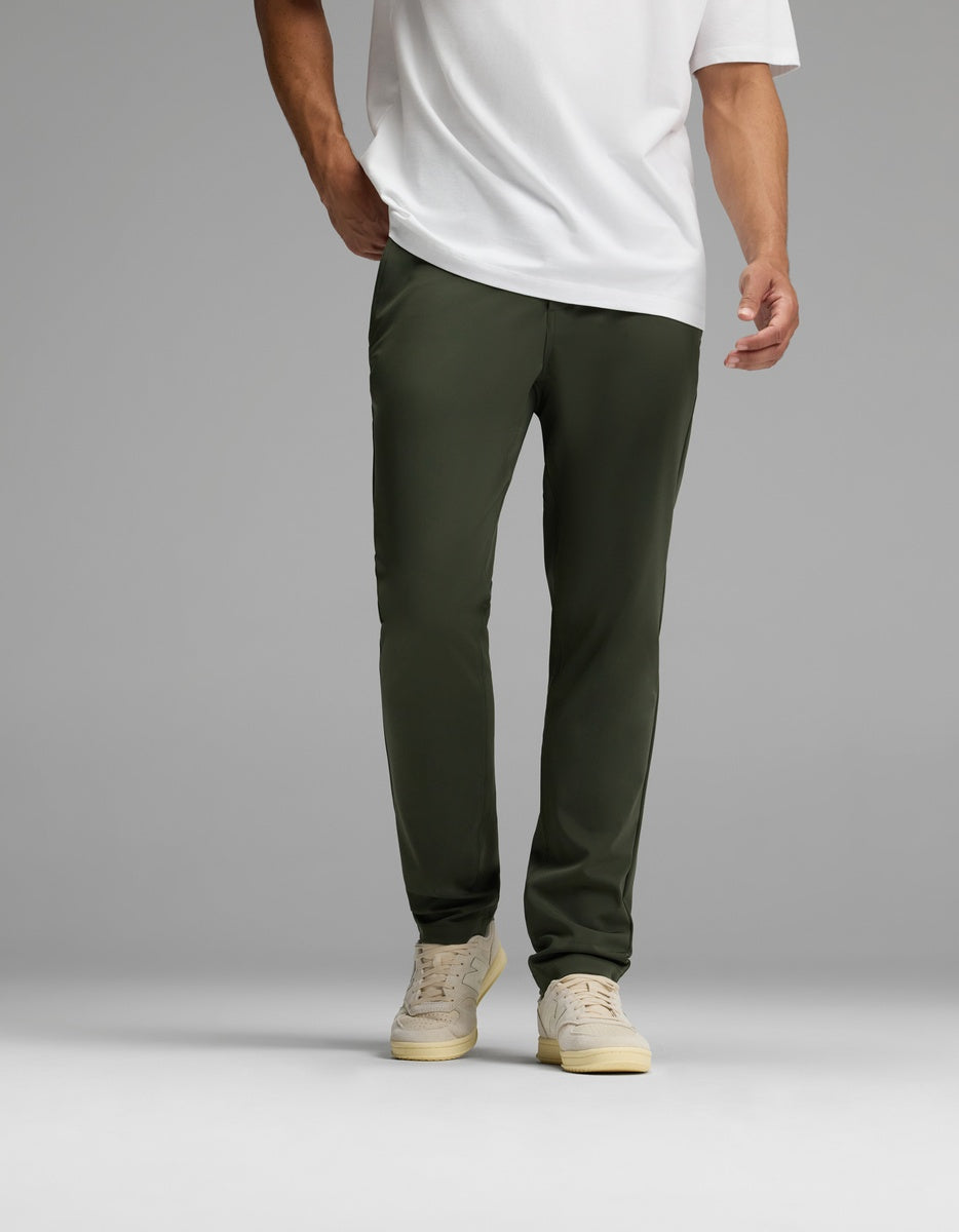 A person wearing Cozy Earth’s Men’s Everywhere Pant in olive green is pictured standing against a plain gray background. The image is cropped at the shoulders, focusing on the lower torso and legs.|Color:Olive