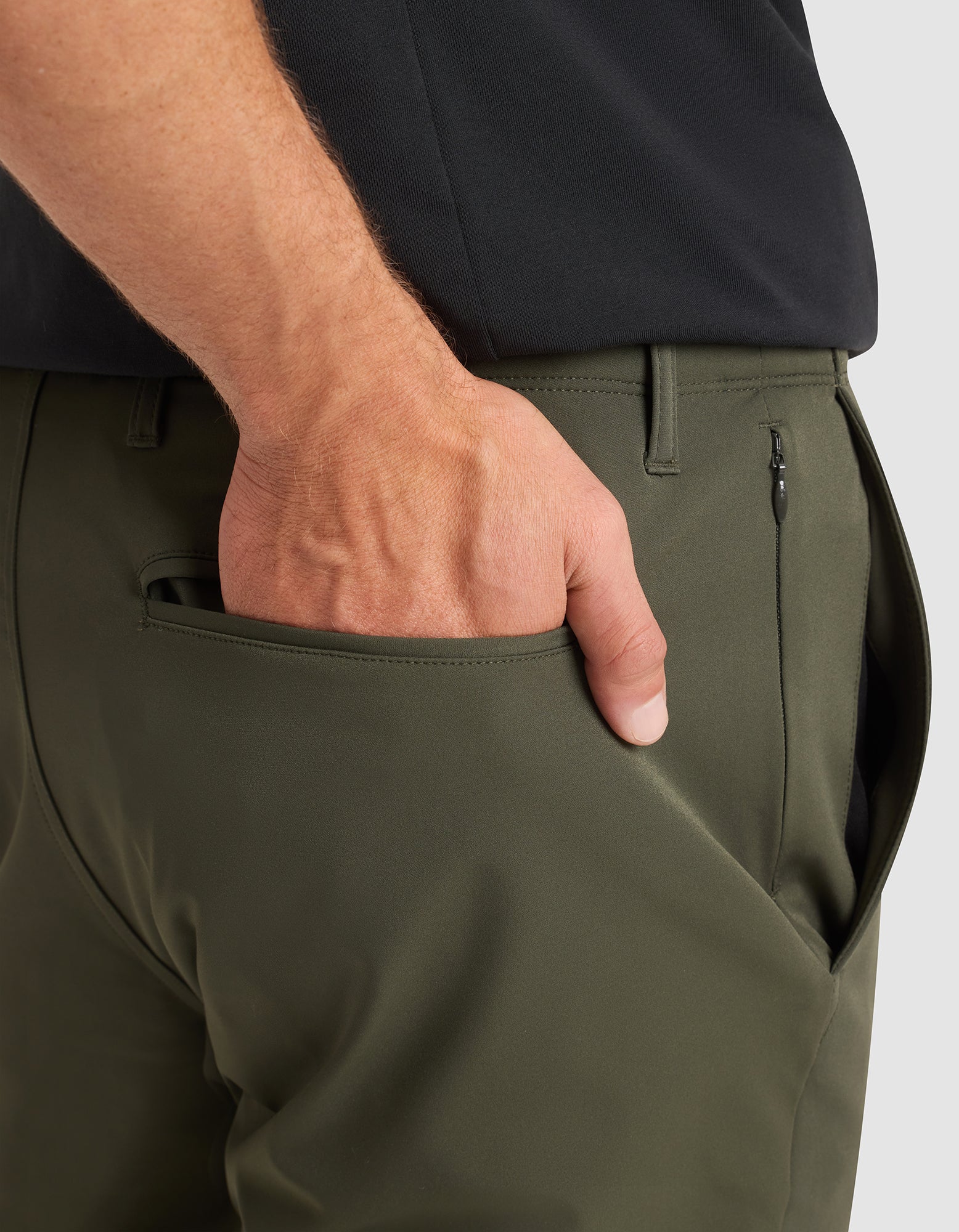 A close-up of a person wearing Cozy Earth’s Men's Everywhere Pant in olive green and a black shirt, with their right hand in the pants pocket. 