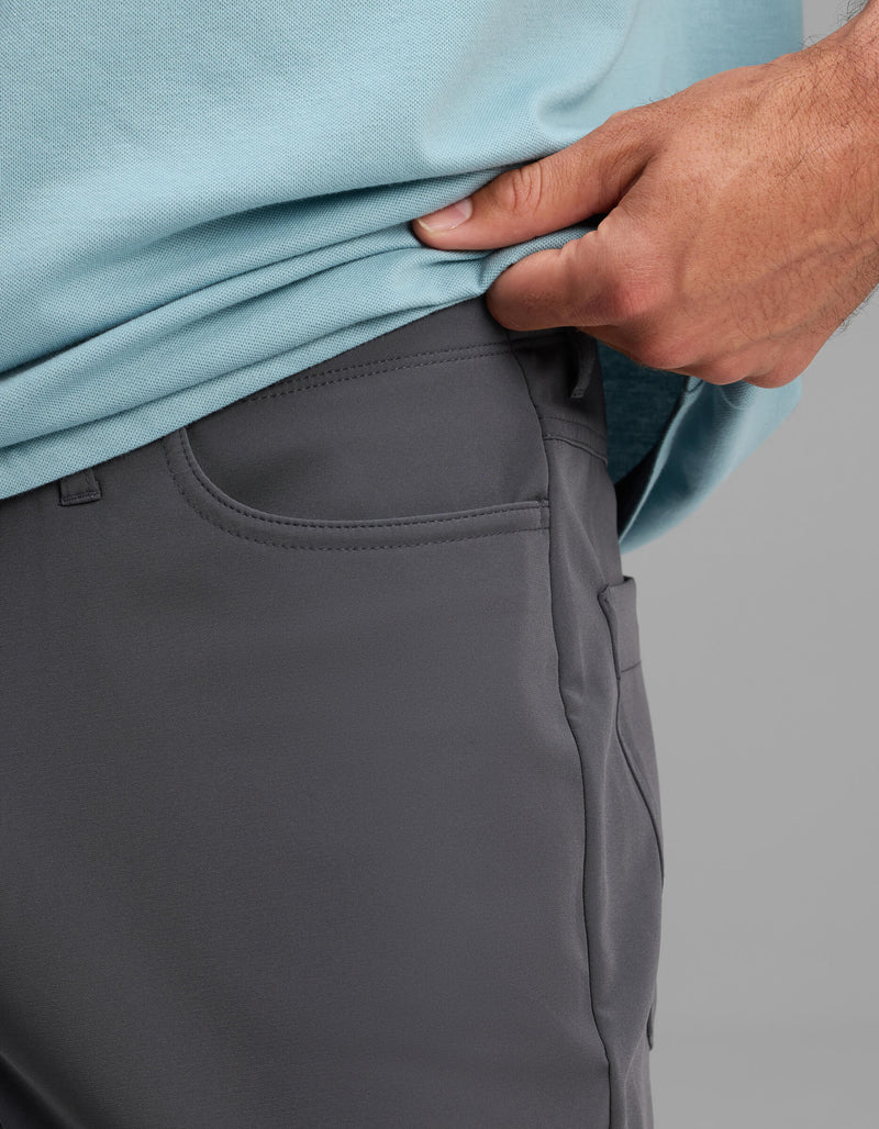 A close-up of a person wearing Cozy Earth's Men's Everywhere Pant - Relaxed Fit in gray, paired with a light blue shirt, as they lift the shirt slightly to reveal the pants' waistband.
