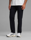A person wears Cozy Earth's Men's Everywhere Pant - Relaxed Fit in black, paired with a white t-shirt and white sneakers with black accents. Only the lower half of the body is visible against a plain gray background.|Color:Jet Black