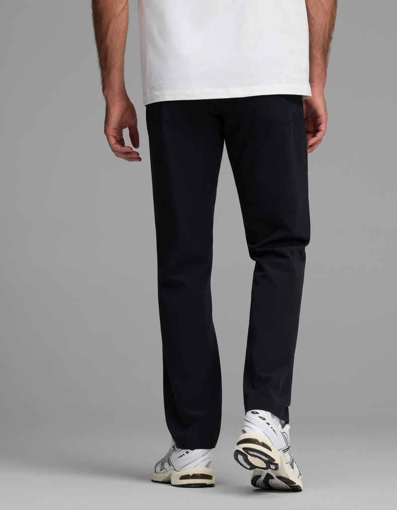 A person stands with their back to the camera against a plain gray background, wearing Cozy Earth’s Men's Everywhere Pant - Relaxed Fit, paired with a white T-shirt and white sneakers.