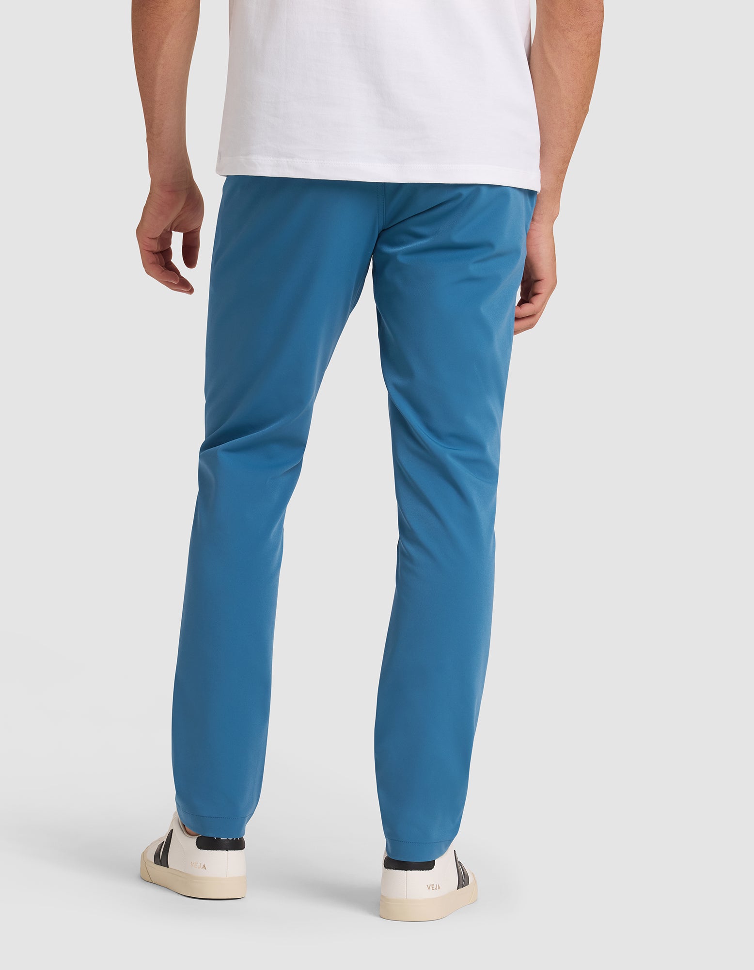 A person models the back view of the Cozy Earth Men's Everywhere Pant, paired with a white t-shirt and white sneakers with dark accents, against a plain light background.  