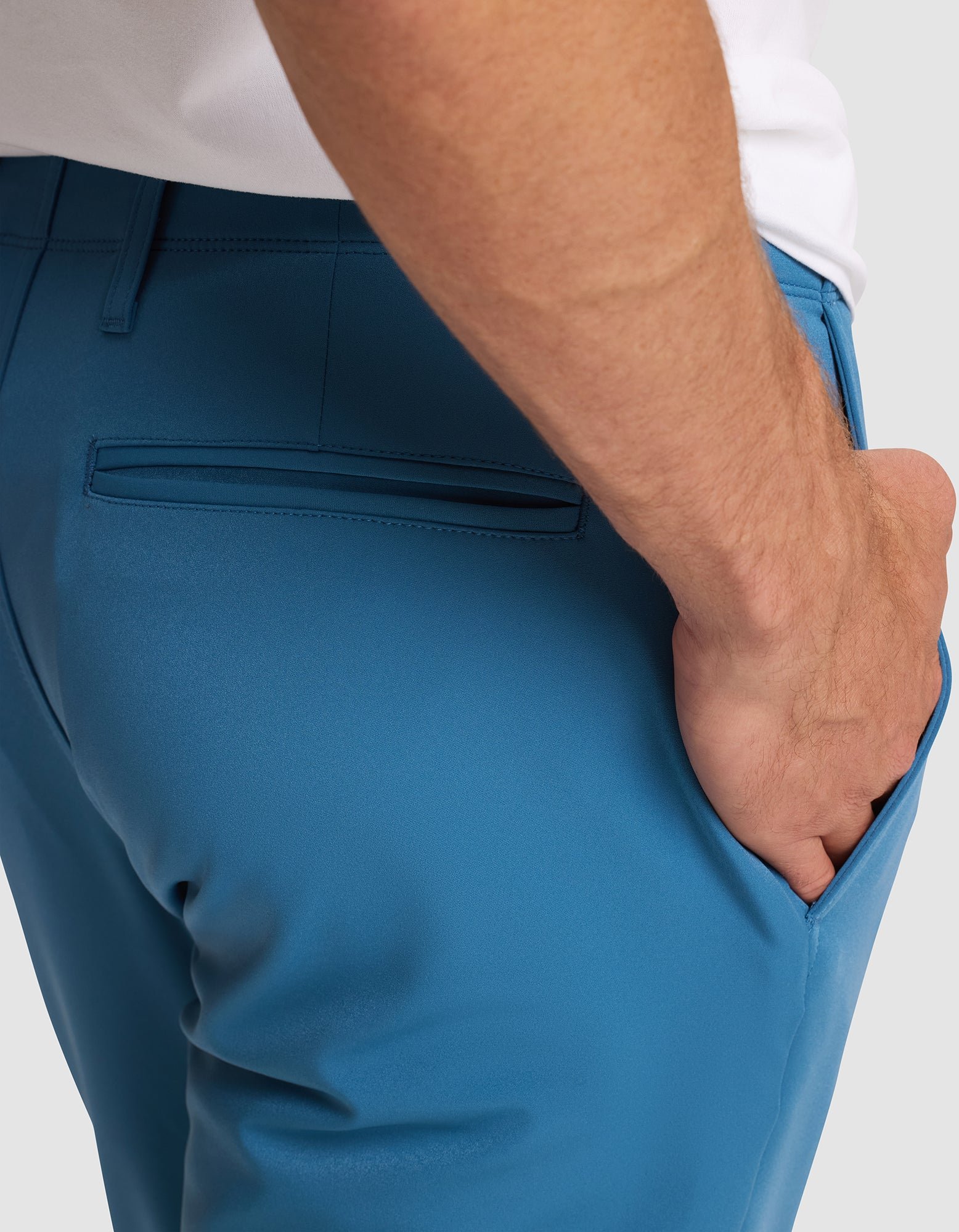 A man wearing Cozy Earth’s Men's Everywhere Pant in bright blue, shown from the waist down with his right hand in his pocket. The pants feature a back welt pocket and a white shirt is partially visible.   