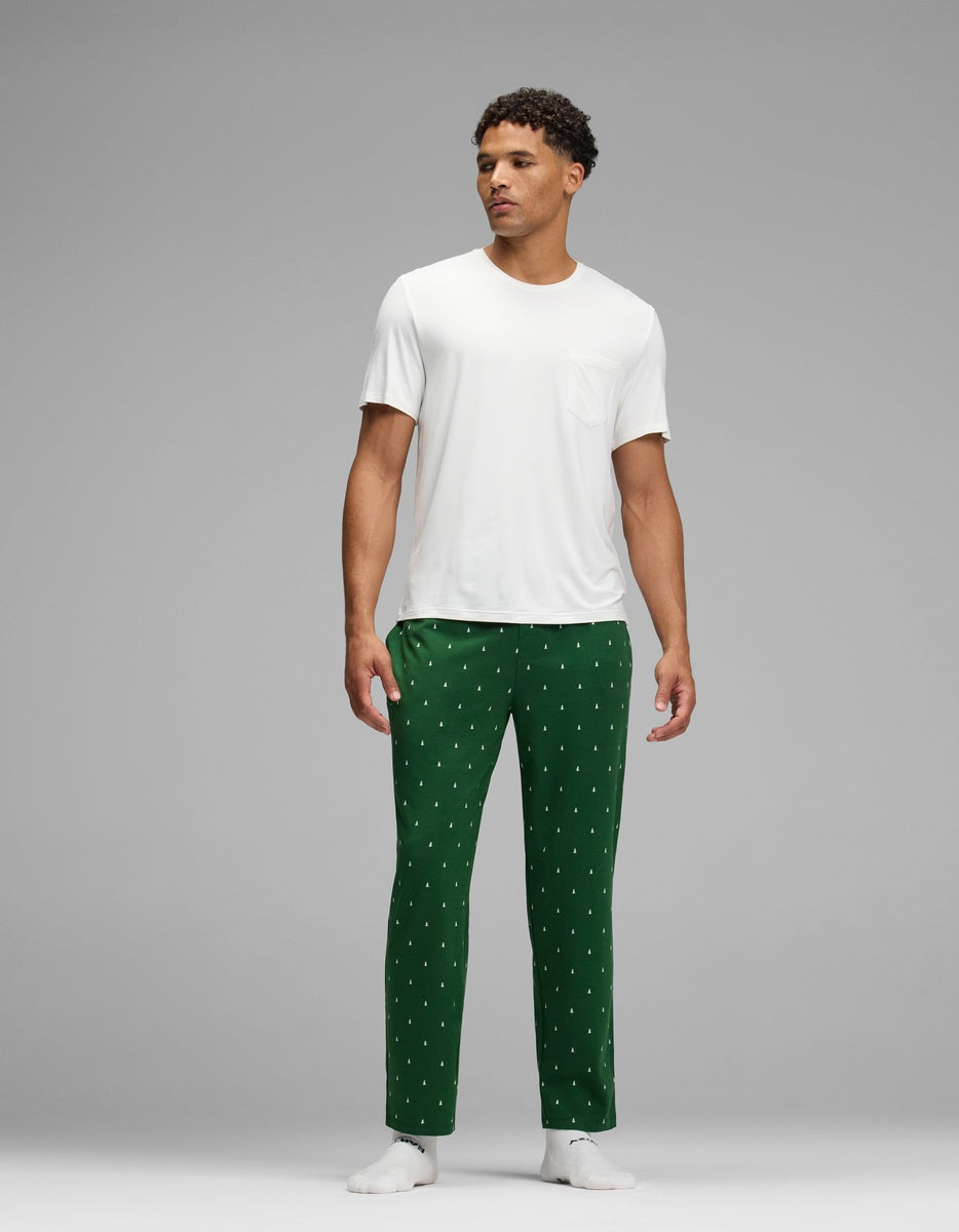 A man wearing a white t-shirt and green Men’s First Layer Pajama Pant with a small white tree pattern.