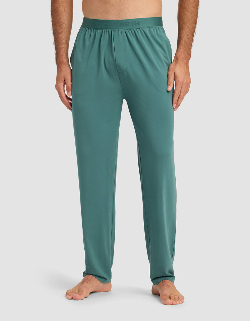 A man stands barefoot wearing Cozy Earth's Men's First Layer Pajama Pant in teal with an elastic waistband and no visible pockets, shown from the waist down against a plain light background.