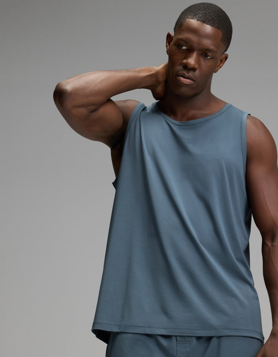 A man wearing the Cozy Earth Men’s First Layer Pajama Tank and matching shorts in Dawn stands against a plain gray background, with one hand resting behind his neck.|Color:Dawn