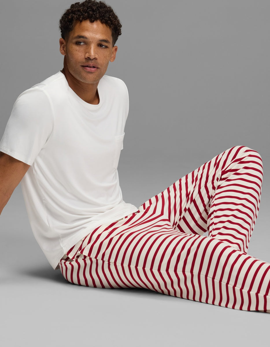 A man wearing a white t-shirt and red and white striped Men’s First Layer Pajama Pant by Cozy Earth sits on the floor.